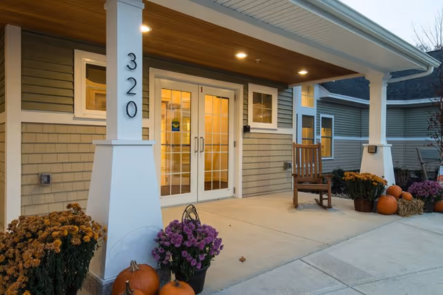Exterior entrance of Avita of Stroudwater with a porch, rocking chair, pumpkins, and planters.