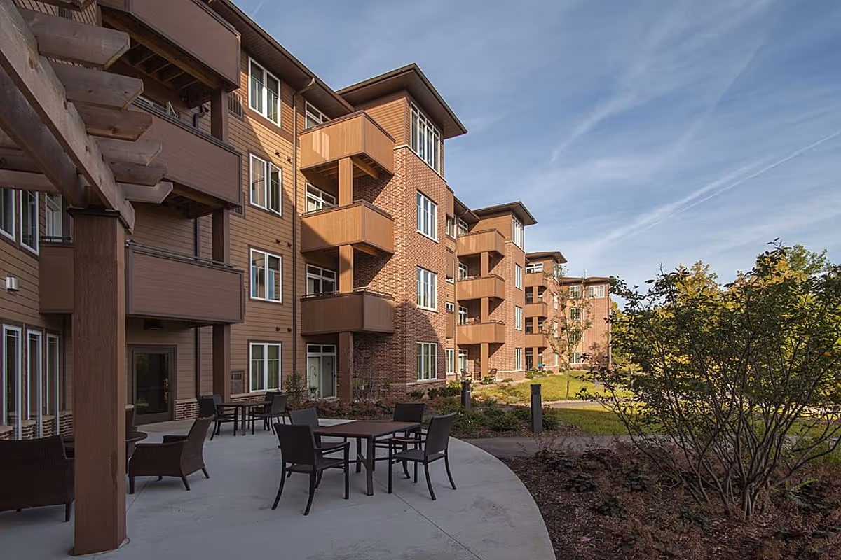 Outdoor courtyard of a multi-story brick and wood-clad building with patio tables, chairs, balconies, and landscaping.