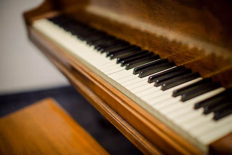Close-up view of the keyboard of a wooden piano with a matching wooden bench in front of it.