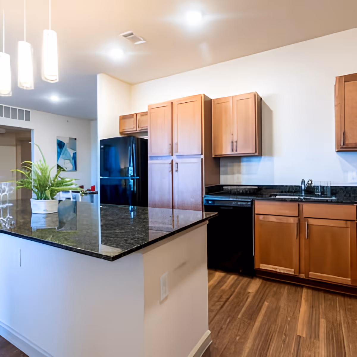 Modern kitchen featuring a dark granite island, wooden cabinets, a black refrigerator, sink, and hardwood floors.