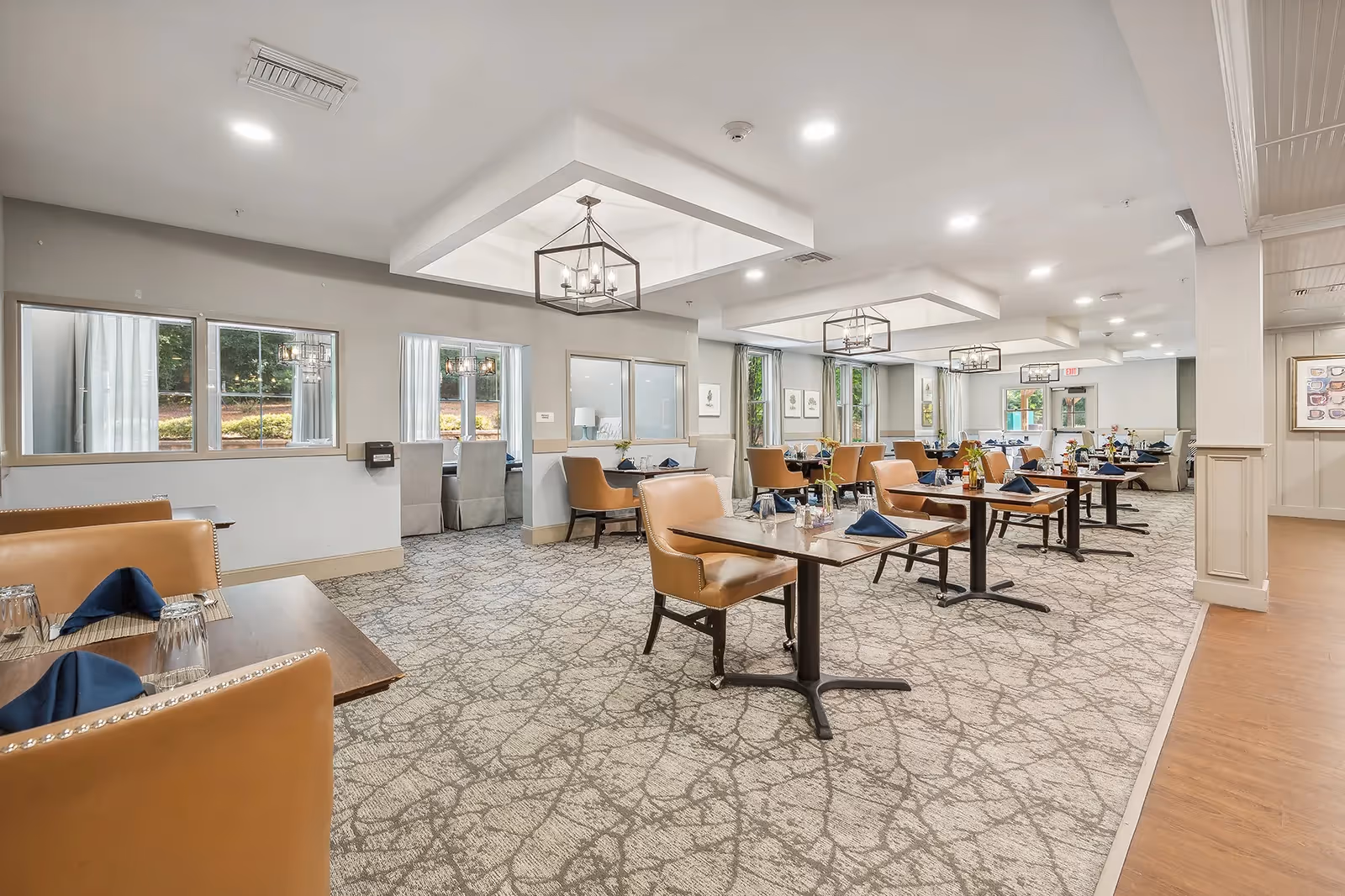 Bright communal dining room with tables set with napkins and leather chairs under modern light fixtures.