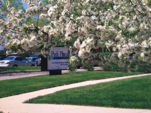 Park Plaza Retirement Center sign beside blooming trees along a sidewalk.