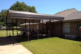 Exterior view of a brick senior facility with a shaded patio and green lawn.