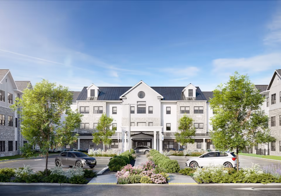 Front exterior view of a large, modern senior living facility named Azalea at Cinnaminson, featuring a three-story building with white and stone facade, black roof, multiple windows, a covered entrance, landscaped greenery, trees, and parked cars in front under a clear blue sky.