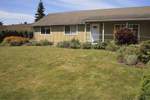 Front view of a single-story beige senior facility with lawn and shrubs.