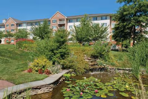 Exterior view of Ann's Choice Retirement Community with a pond and lush landscaping