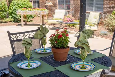 Outdoor patio table set for four with folded green napkins, potted centerpiece, and lounge chairs.