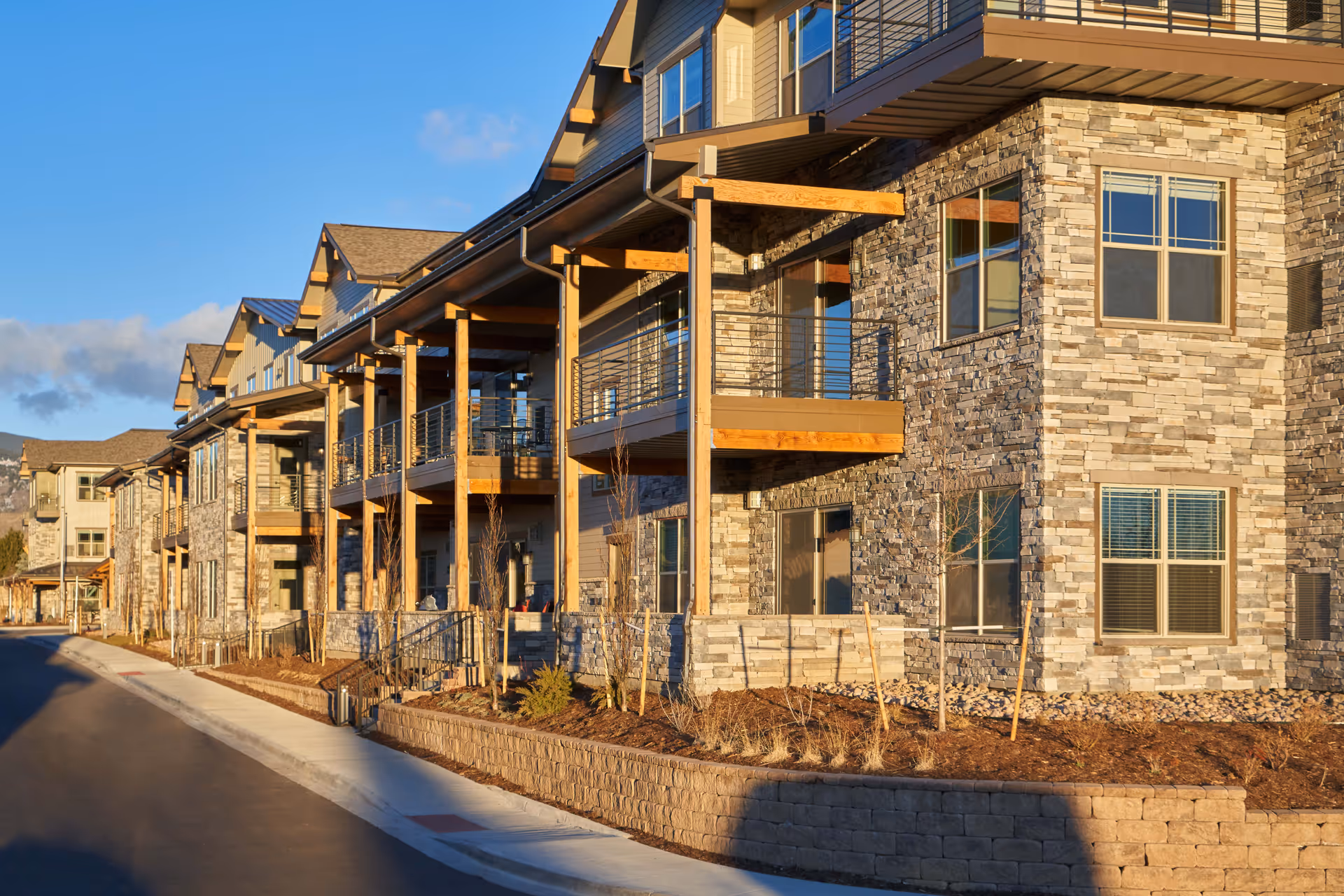 Stone-and-wood senior living building with multiple balconies facing a sunny street.