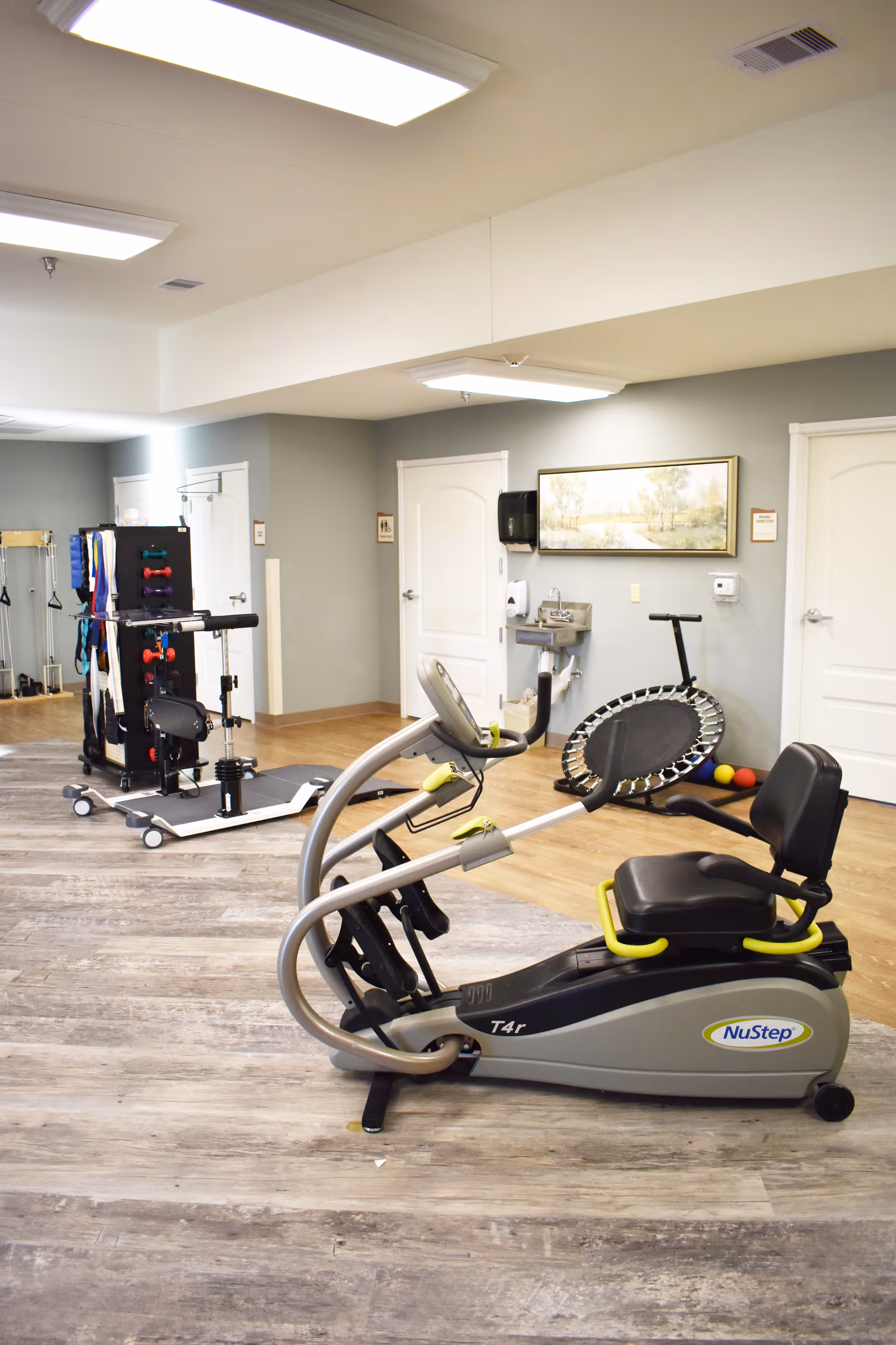 Indoor therapy/exercise room with a NuStep recumbent cross trainer, mini trampoline, and other rehabilitation equipment.