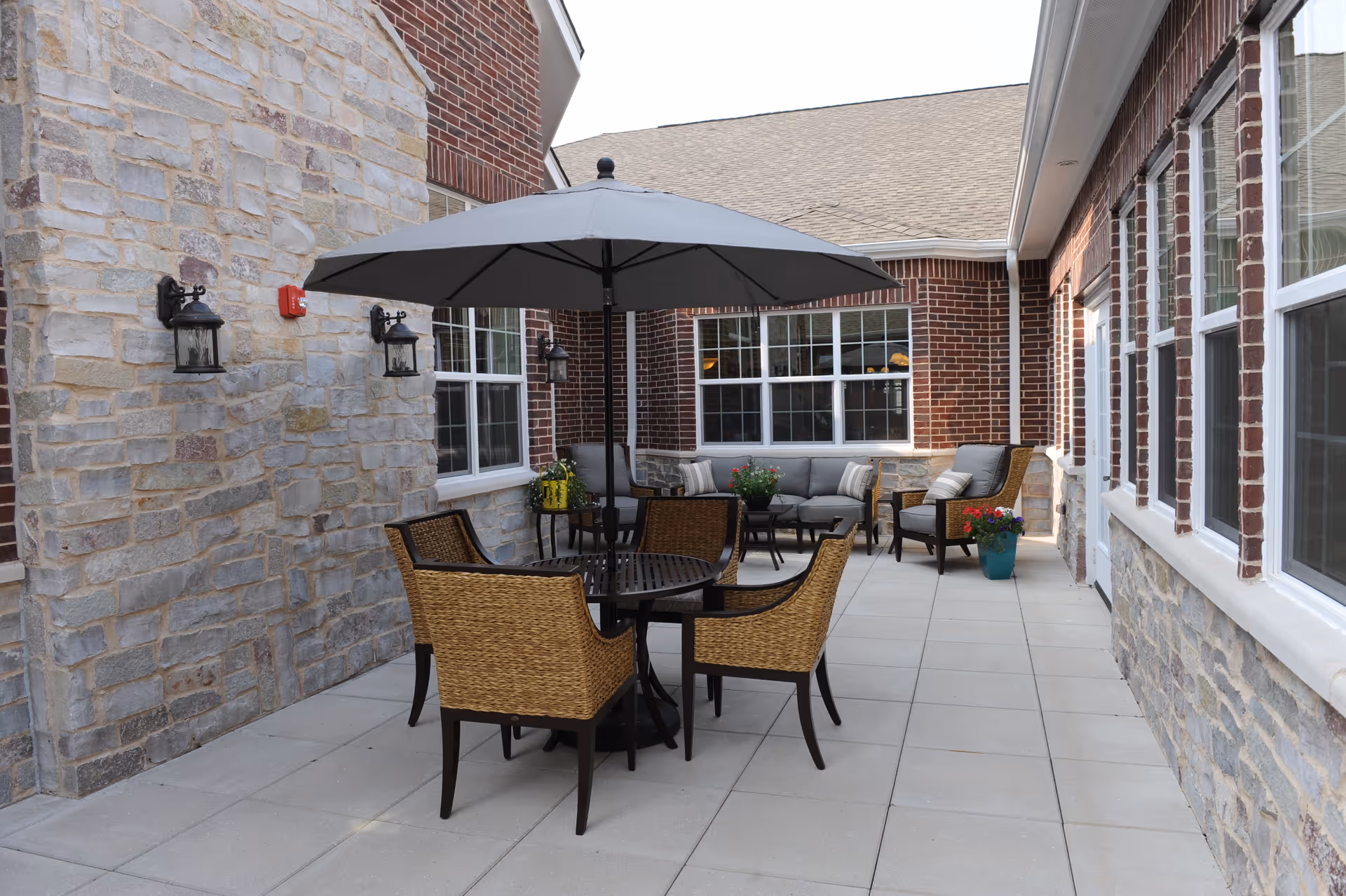 Outdoor patio with a round table, umbrella, wicker chairs, and cushioned seating along brick and stone walls.