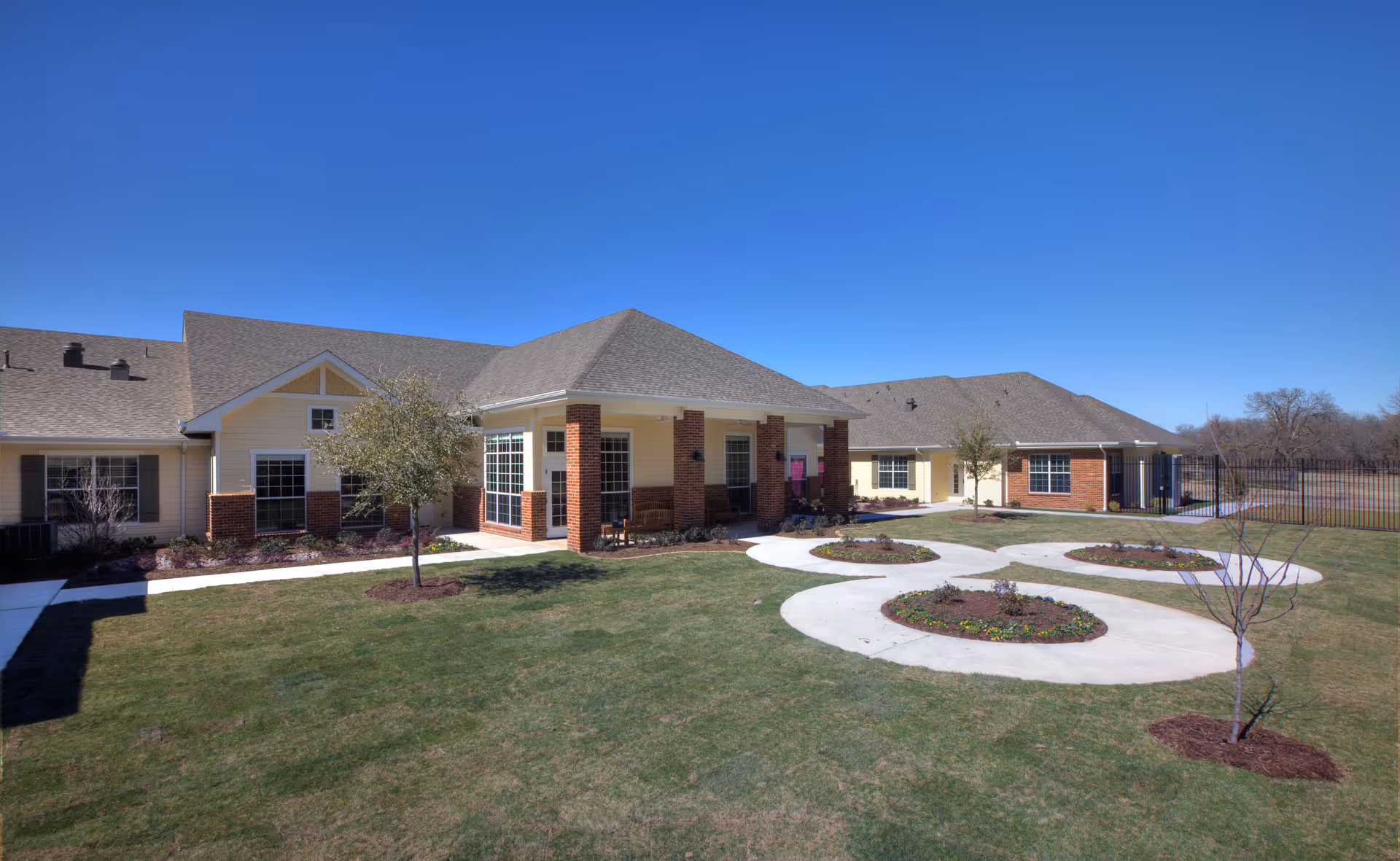 A single-story senior living facility with beige siding, brick columns, and circular walkways.