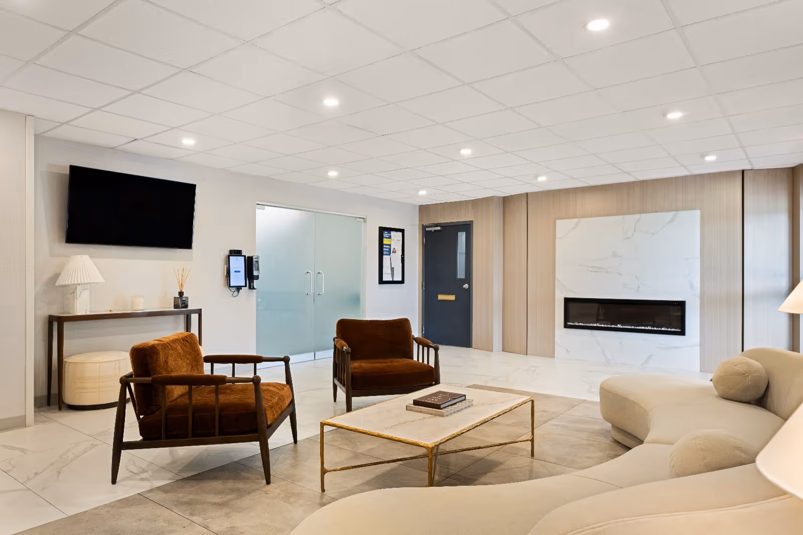 Modern lounge area with curved sofa, armchairs, coffee table, wall-mounted TV and a fireplace.