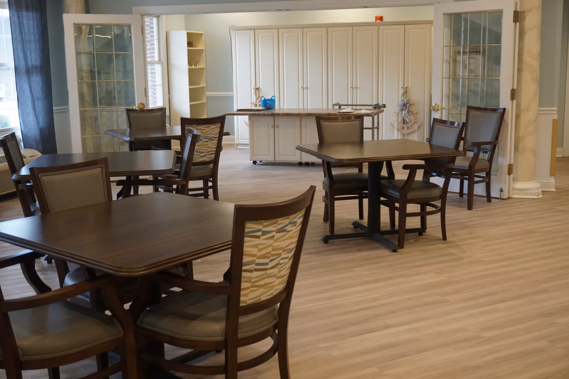 Empty dining area with several wooden tables and chairs and a cabinet/island against the back wall.