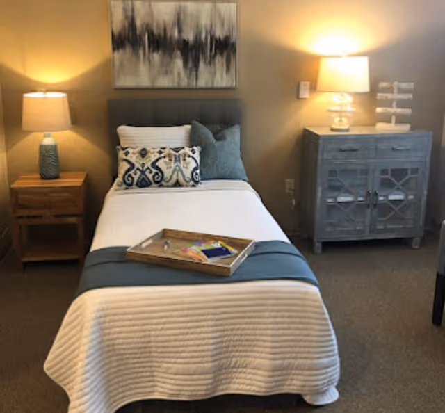 Neatly made single bed with decorative pillows and a tray, flanked by nightstands and lamps in a cozy bedroom.