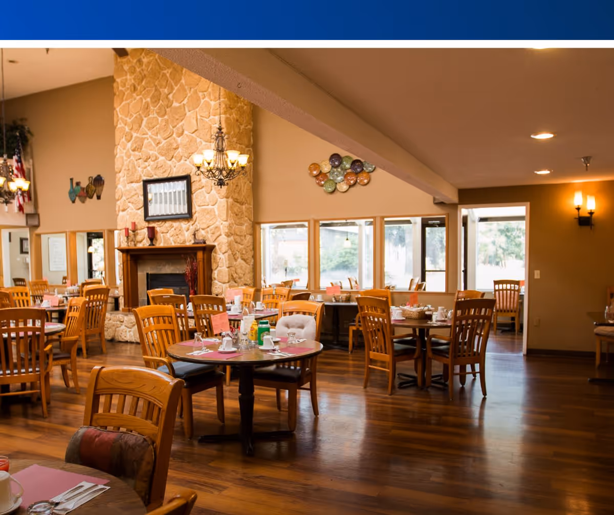 Spacious dining room with wooden tables and chairs, set place settings, a stone fireplace and large windows.