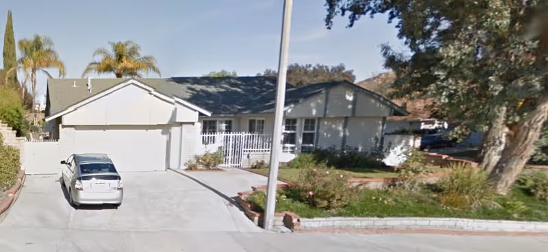 Single-story residence-style facility with driveway, parked car, and landscaped front yard.
