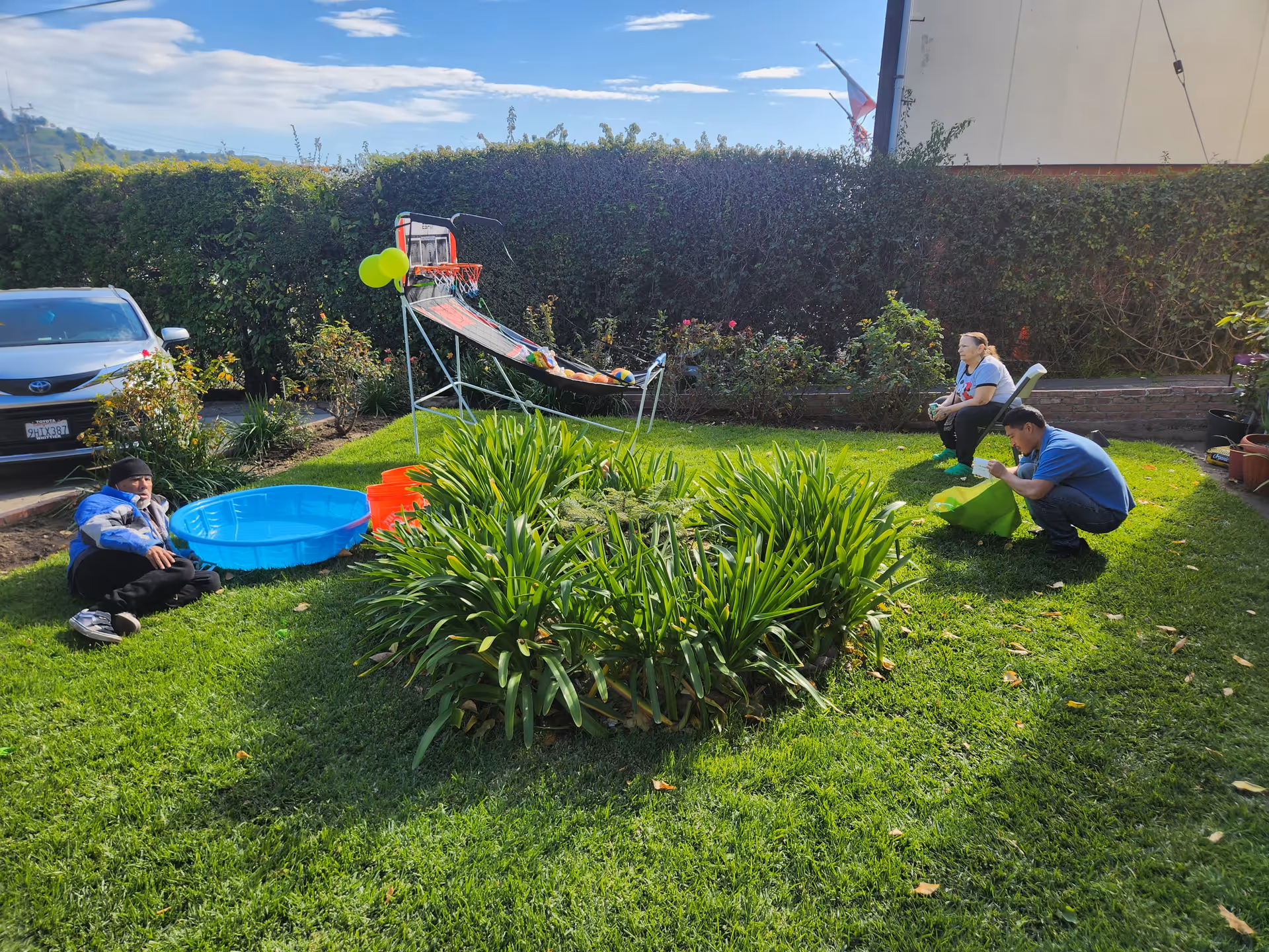 Three individuals engaging with a small blue pool and greenery in a garden setting.