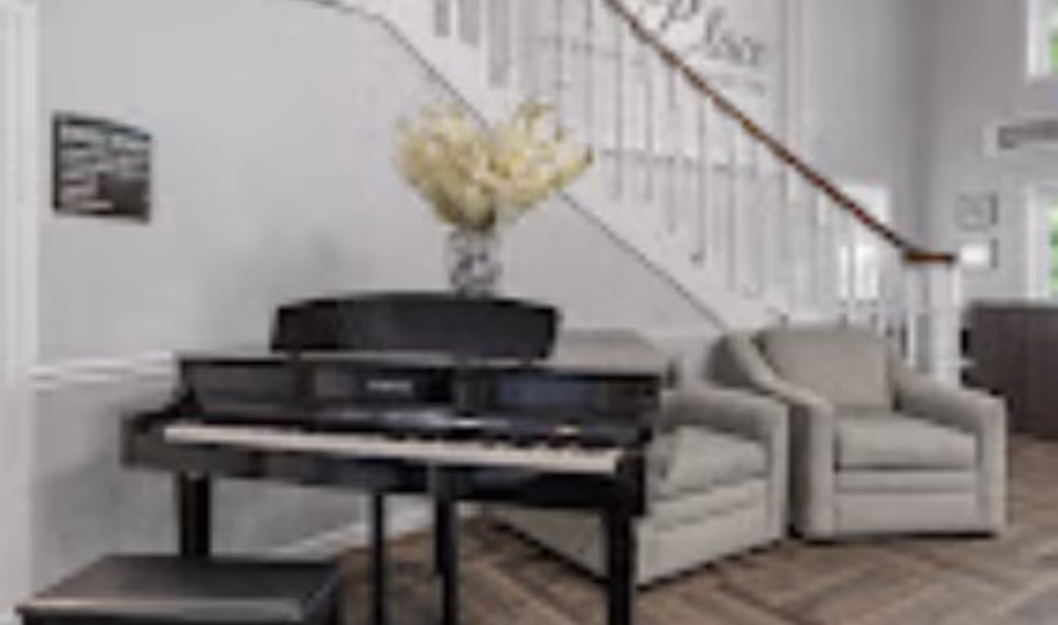 Interior common area with an upright piano, a vase of flowers, two armchairs, and a staircase in the background.