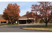 Exterior view of a single-story brick building with a covered entrance, surrounded by trees with autumn foliage and a curved driveway in front.