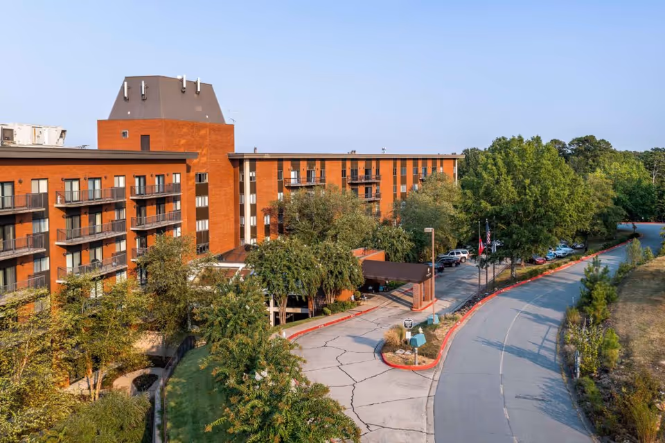 Exterior view of Woodland Heights Senior Living building with balconies, trees, and curved driveway.