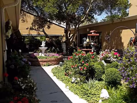 Outdoor courtyard garden with colorful flowers and a fountain near a beige building.