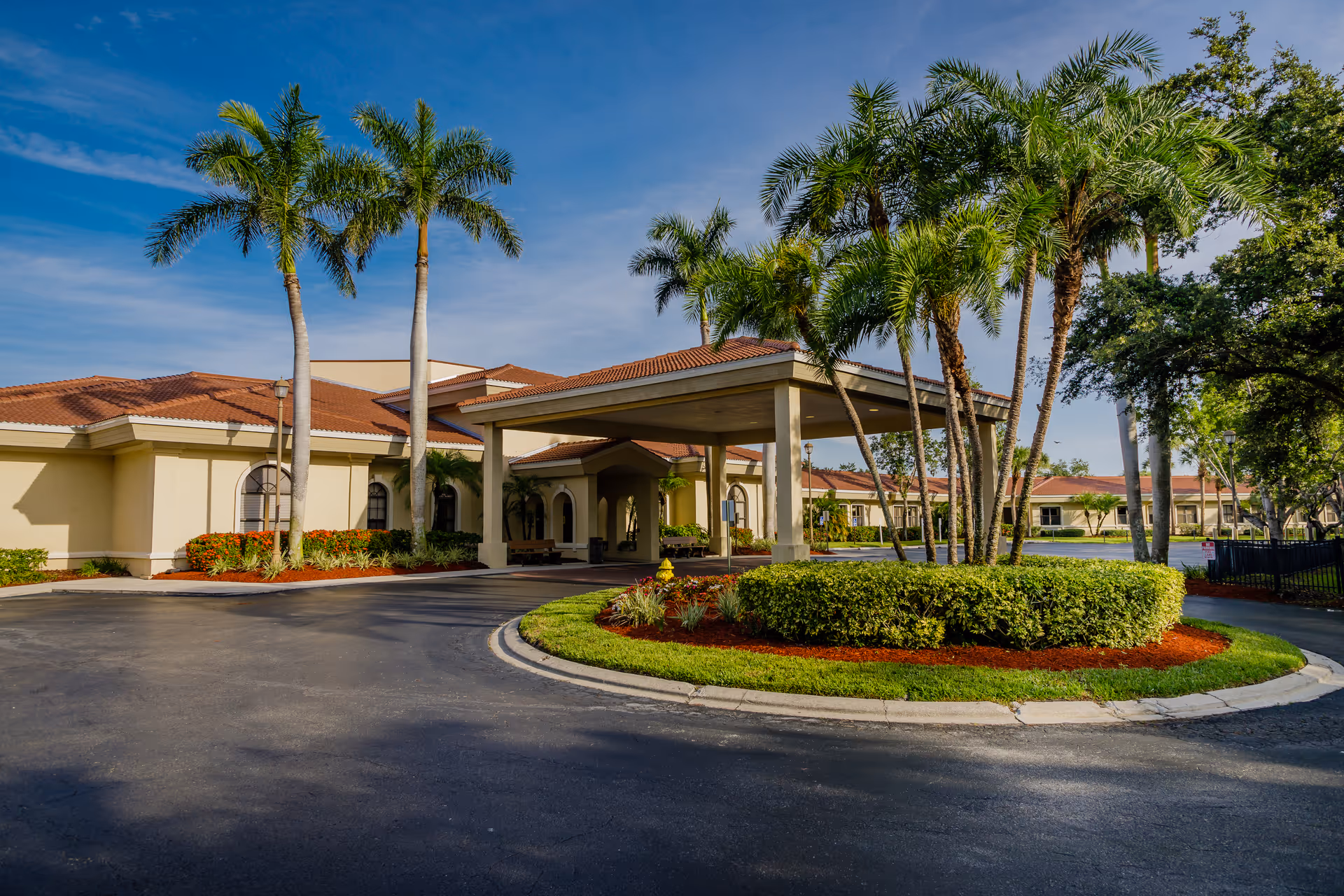 Front entrance and porte-cochère of a low-rise healthcare building surrounded by palm trees and a landscaped circular driveway.