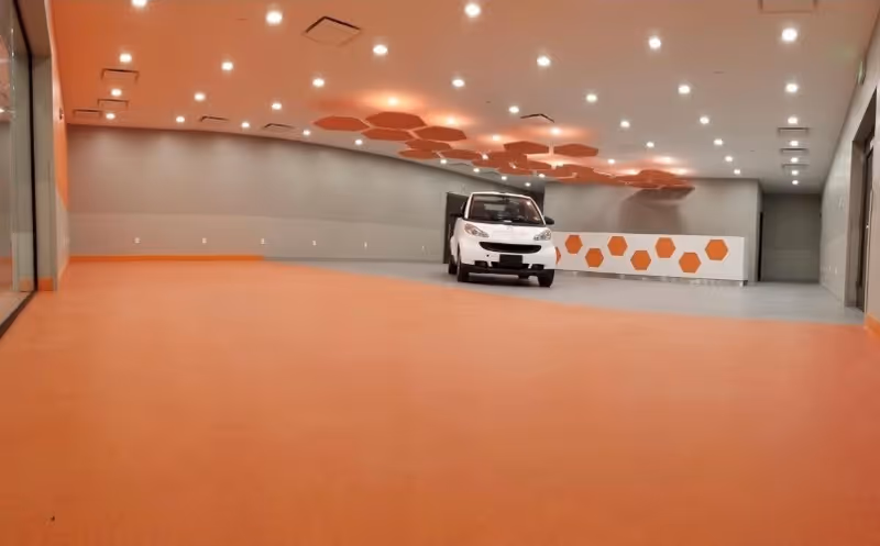 Large bright interior room with an orange floor and ceiling hexagon accents and a small white utility vehicle near a hexagon-decorated counter.