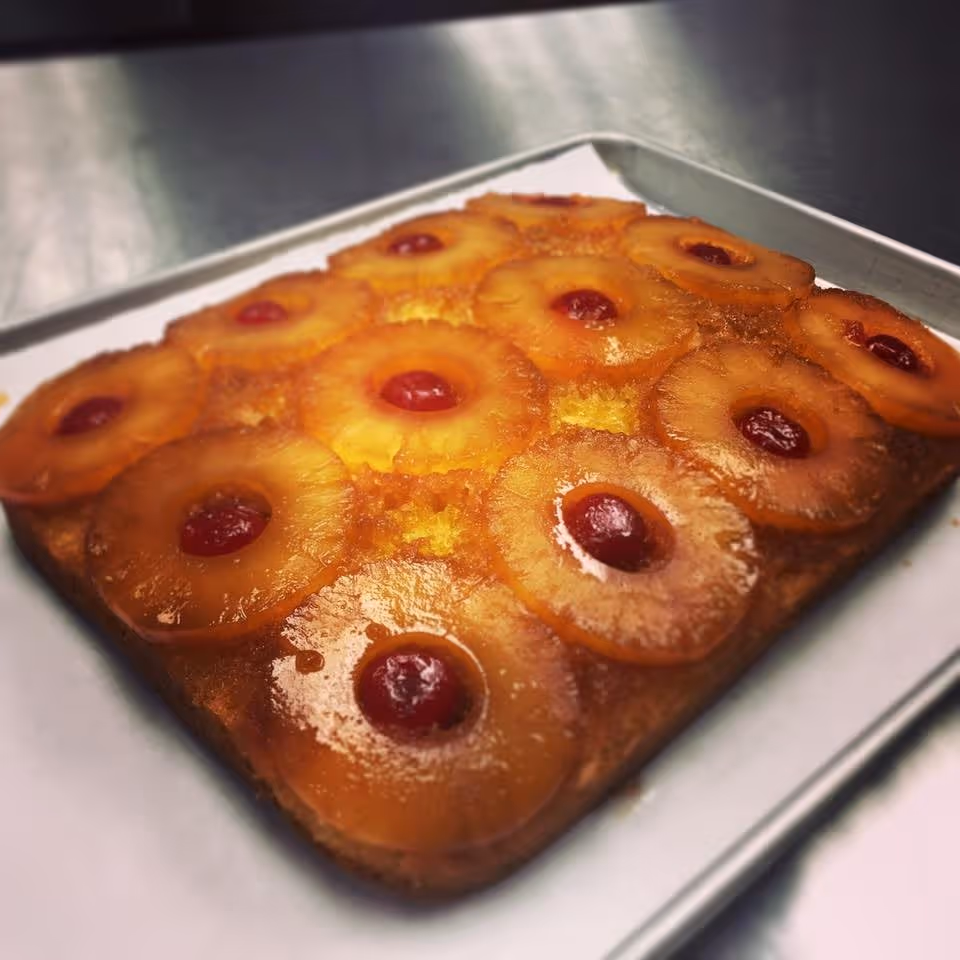 A freshly baked pineapple upside-down cake on a baking tray, topped with pineapple rings and maraschino cherries in the center of each ring.