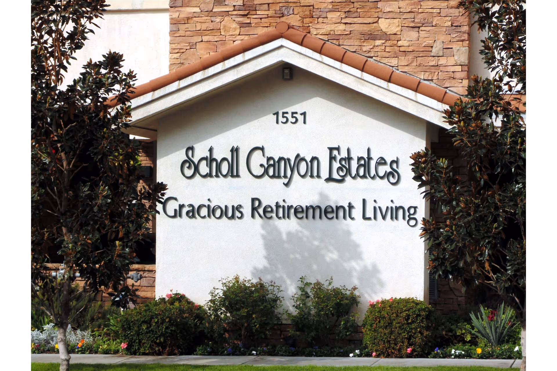 Exterior sign for Scholl Canyon Estates Gracious Retirement Living with landscaped shrubs.