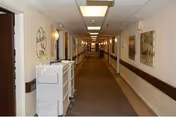 Long interior hallway of a senior living facility with doors, artwork, and overhead lighting.