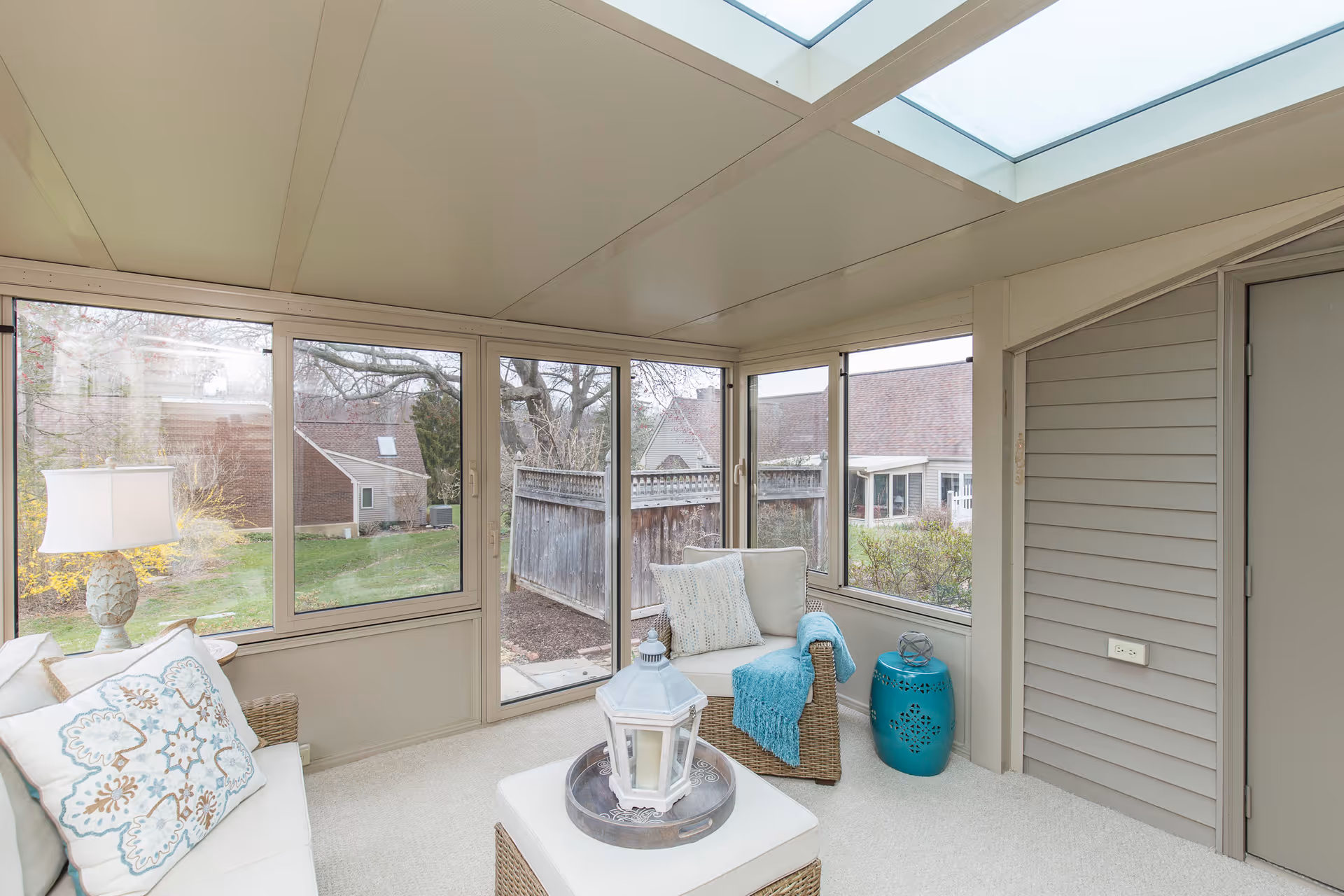 Bright sunroom with wicker seating, skylights, and large windows overlooking a fenced backyard.