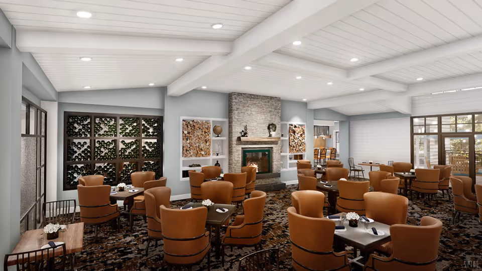 Spacious dining room with multiple tables and orange upholstered chairs, a central stone fireplace, and large windows.