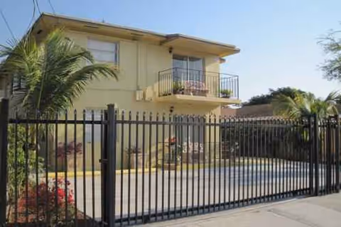 Two-story beige senior living facility exterior with a fenced pool and palm trees.