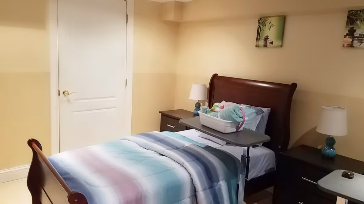 Small furnished bedroom with a single sleigh bed, bedside tables and lamps, an overbed tray holding folded linens.