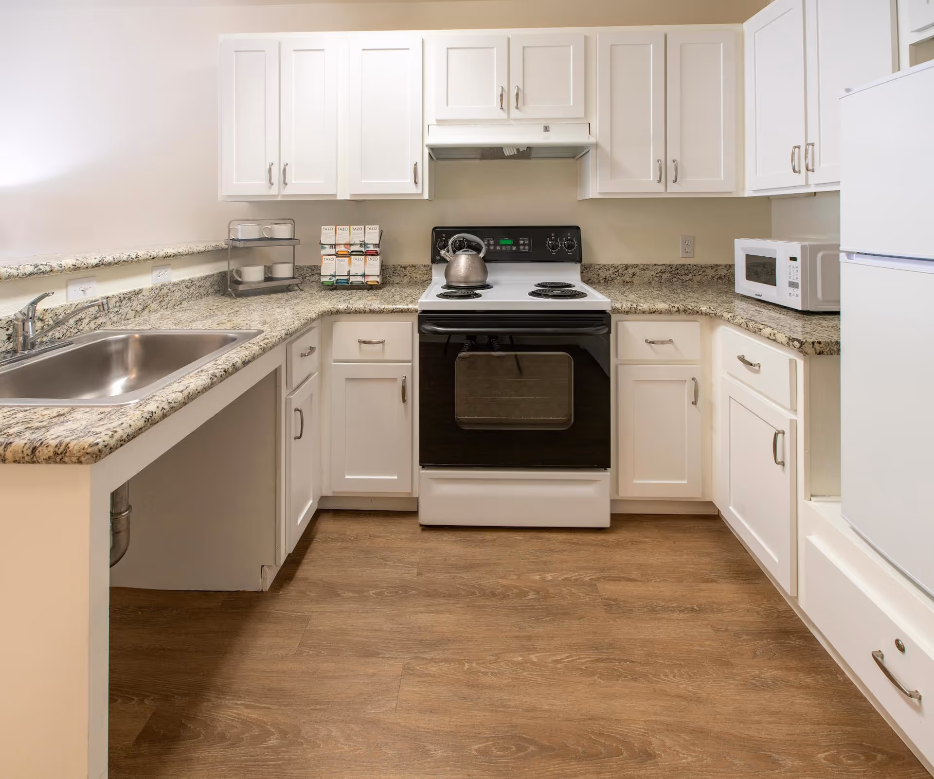 Bright kitchen with white cabinets, granite countertops, a stove, microwave and a stainless steel sink.