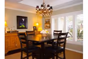 Dining room with a dark wood table and chairs, chandelier, sideboard, artwork on the wall, and windows with white plantation shutters.