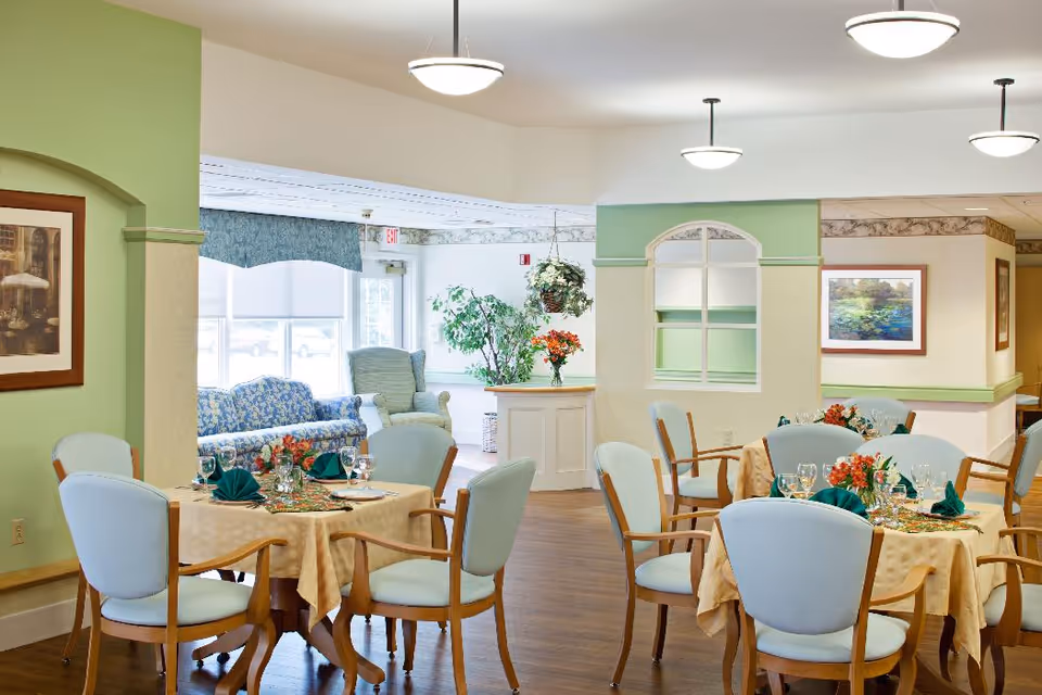 Bright dining room with round tables set for a meal, light blue chairs, and a seating area in the background.