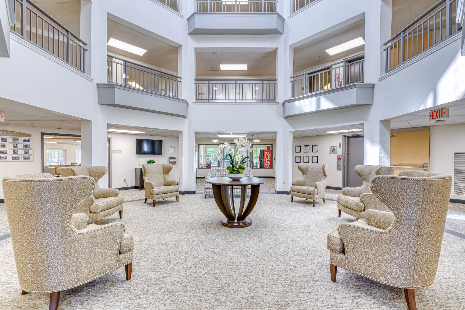 Two-story atrium lounge with wingback chairs arranged around a central table and upper-level balconies.