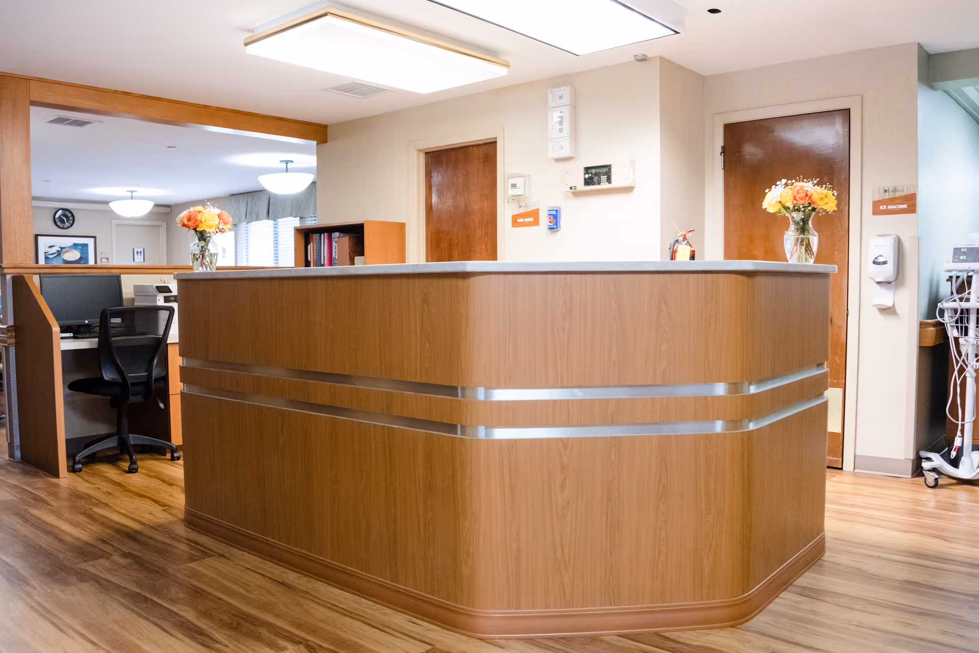Wood-paneled reception desk in an interior office area with chairs, flowers, and office equipment.
