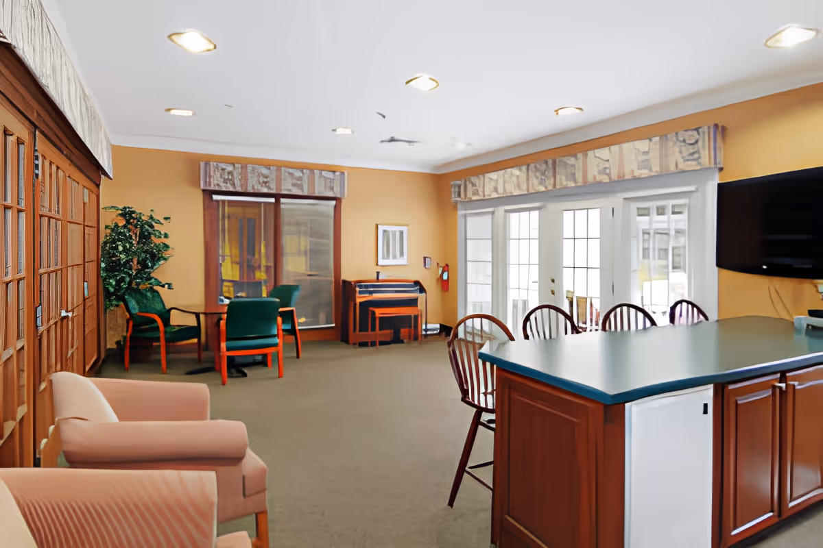 Communal lounge area with seating, a kitchen-style island with bar stools, tables, and large glass doors letting in natural light.