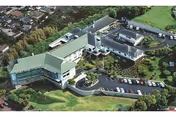 Aerial view of Maunalani Nursing & Rehab Center showing a large, multi-wing building with green roofs surrounded by landscaped grounds and parking lots with several cars.