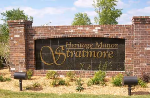 Brick entrance sign reading Heritage Manor Stratmore with landscaped shrubs in front