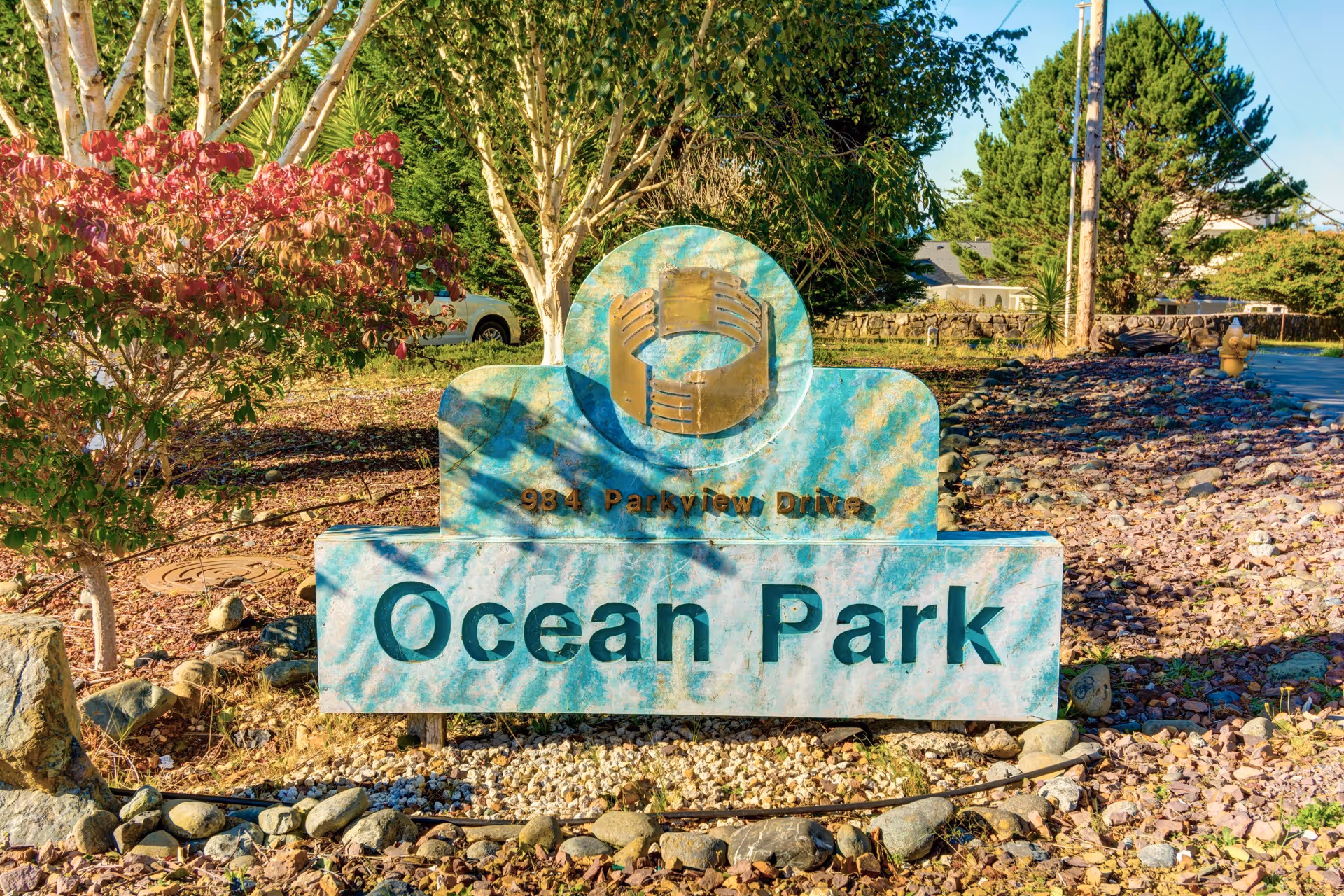 Turquoise entrance sign that reads 'Ocean Park' set among rocks, shrubs, and trees.