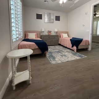 Two twin beds with pink bedding and navy throws flank a dresser in a bright bedroom.