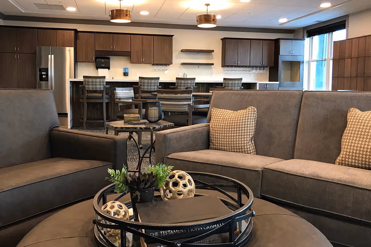 Modern communal lounge with sofas, a round coffee table and a kitchenette/bar with high stools in the background.