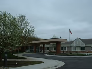 Exterior view of a senior living facility entrance with a covered driveway and flag.