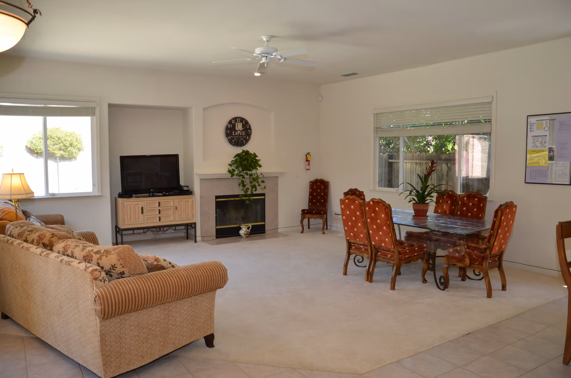 Bright, spacious common room with a sofa and TV by a fireplace and a dining table with upholstered chairs.