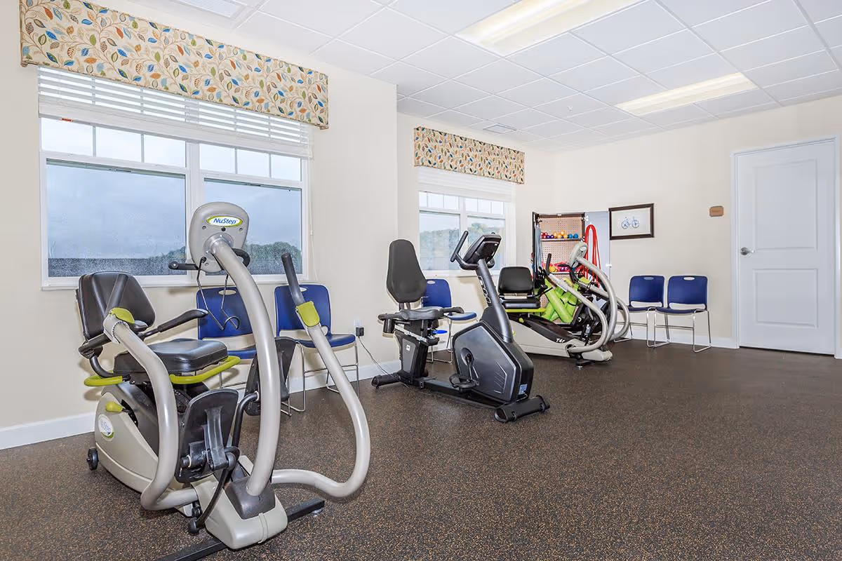 Fitness room with stationary bikes, exercise equipment, and chairs near windows.