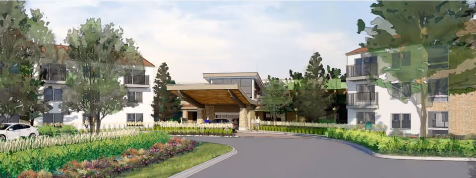 Rendered exterior view of a senior living community entrance with a circular driveway, porte-cochere, landscaped beds and three-story residential wings.