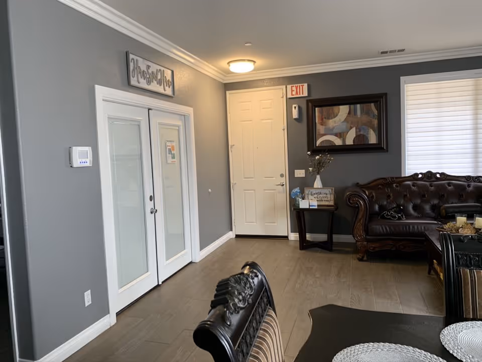 Interior common living area with a leather couch, dining chairs and table, side table, and an entrance door against gray walls.